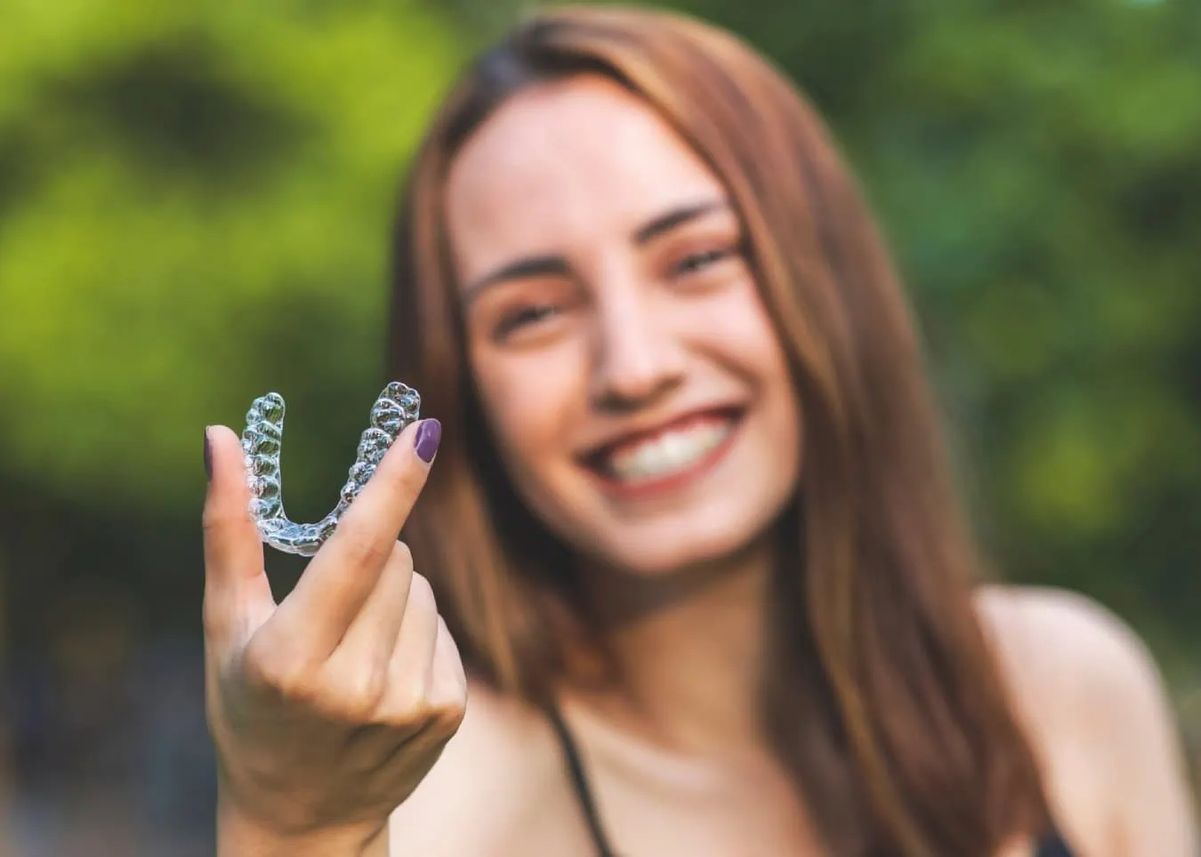 Woman smiling and holding clear aligner tray, illustrating invisible orthodontic treatment.