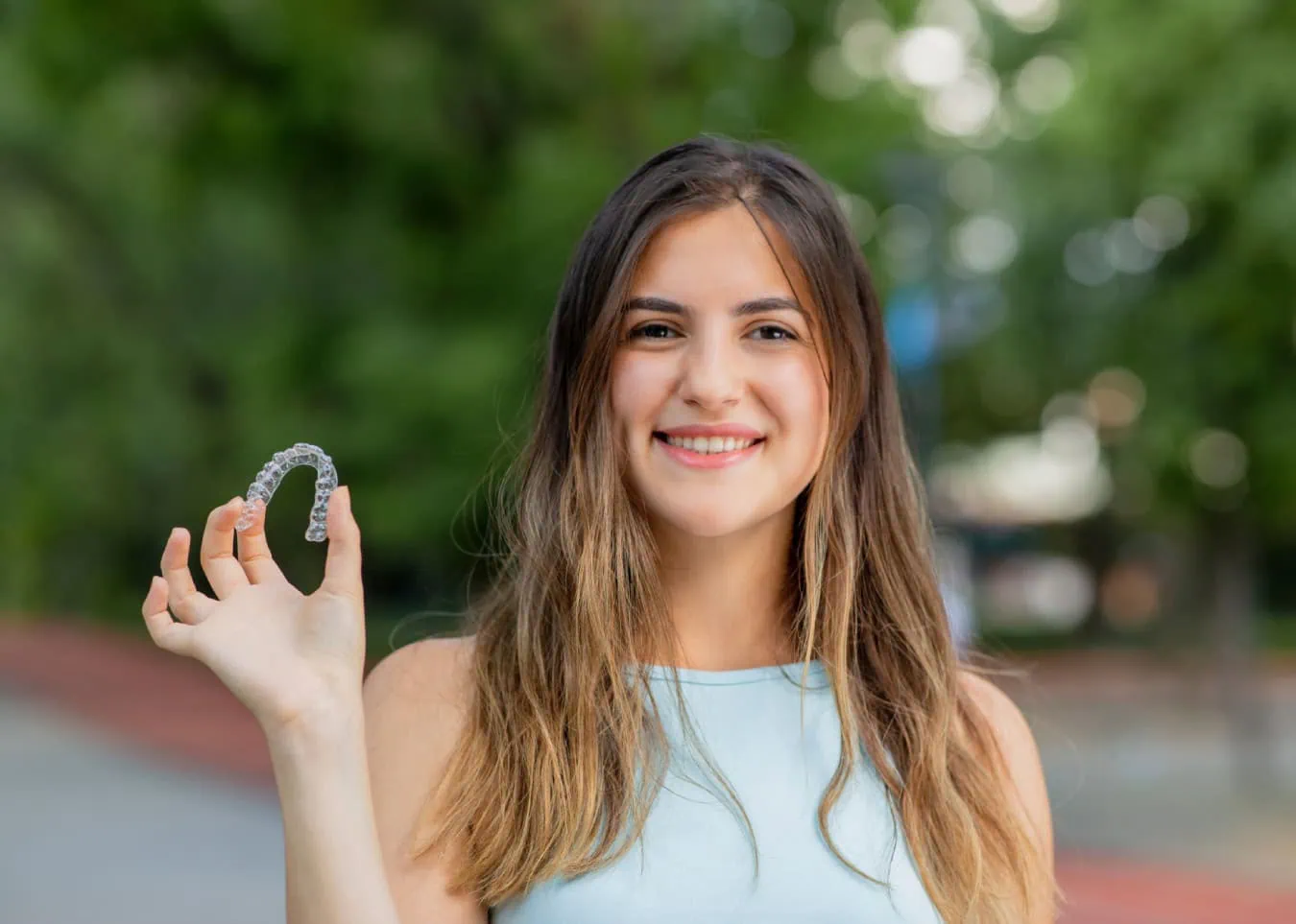 Smiling woman holding clear aligner showcasing discreet teeth straightening treatment.